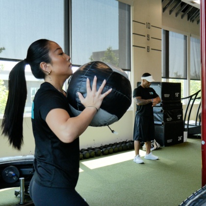 a personal trainer throws a weighted ball during a workout with a gym member at the fitness equation gym in va